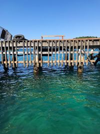 Wooden posts in sea against clear blue sky