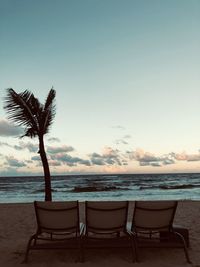 Empty chairs on beach against sky