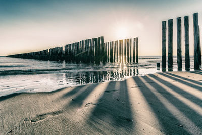 Wooden posts on beach against sky during sunset