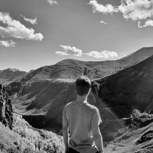 Rear view of man standing on mountain against sky