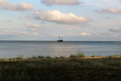 Distant view of sailing ship in sea against sky