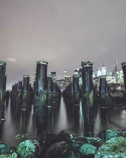 Mooring post in water with modern building against sky at night