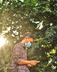 Young man using mobile phone while standing on tree