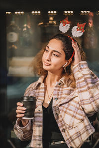 Portrait of young woman standing in front of a coffeeshop with a takeaway coffee in hand