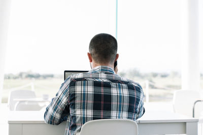 Rear view of man sitting on window