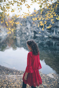 Beautiful curly hair girl in a red dress walking by the lake, looking away from the camera