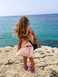 Rear view of girl looking at seascape while standing on coastline