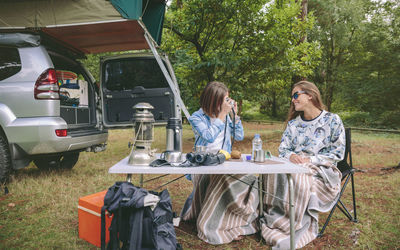 Woman photographing friend through camera at forest