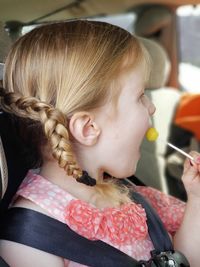 Side view of girl eating lollipop in car