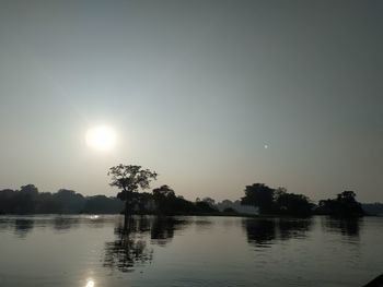 Silhouette trees by lake against sky