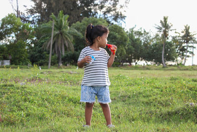 Full length of happy girl holding apple while standing on field