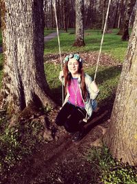 Full length of girl sitting on swing amidst tree trunks