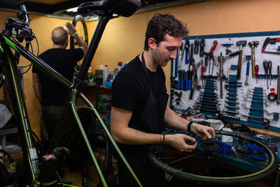 Technician with dirty hands fixing bicycle wheel while working in workshop