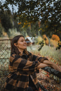 Young woman looking away while standing on tree during autumn