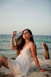 Teenage girl sitting at beach against sky
