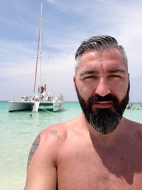 Portrait of shirtless handsome mature man standing in sea against sky