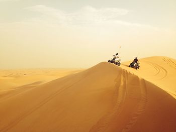 People riding quadbike on sand dune against sky