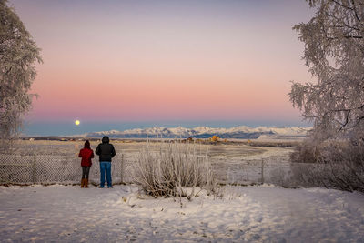 Rear view of couple standing on snow covered land during sunset