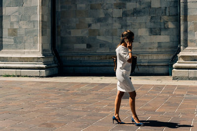 Full length of woman talking on mobile phone while walking on walkway