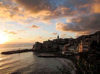 Buildings by sea against sky during sunset