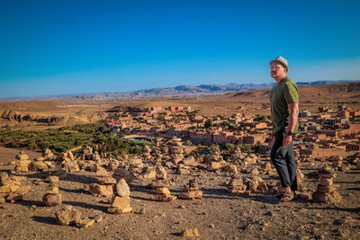 Rear view of man standing on rock against clear blue sky