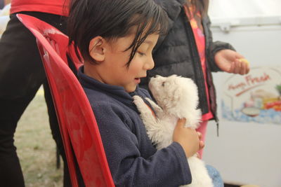 Side view of cute girl holding puppy while sitting on chair