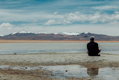 Rear view of man sitting on shore against sky