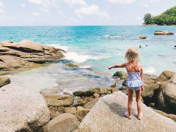 Rear view of girl standing on rock at beach