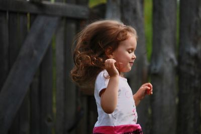 Side view of cute redhead girl walking by wooden fence