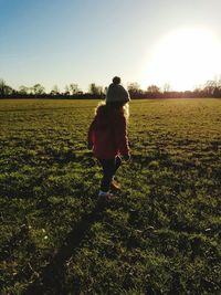 Rear view of girl walking on field against sky