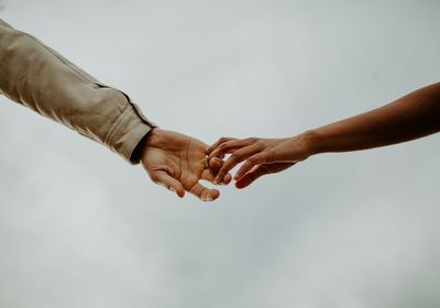 Cropped image of couple holding hands against clear sky