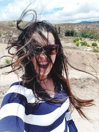 Cheerful woman with tousled hair wearing sunglasses at desert