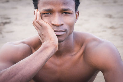 Close-up portrait of shirtless young man sitting at beach