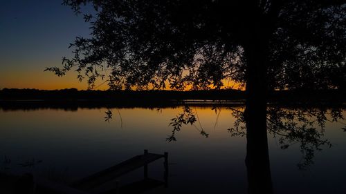 Silhouette tree by lake against sky during sunset