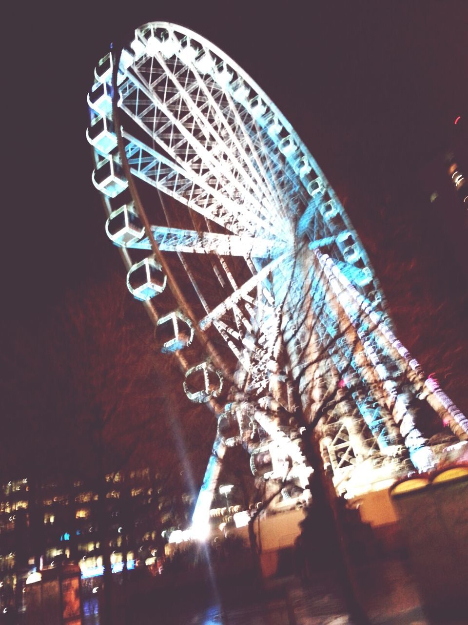 night, illuminated, low angle view, built structure, ferris wheel, arts culture and entertainment, architecture, building exterior, sky, amusement park, amusement park ride, city, tree, clear sky, outdoors, tall - high, no people, lighting equipment, circle, motion