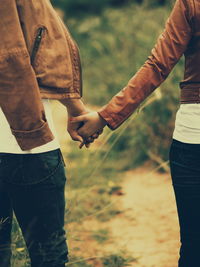 Low section of couple holding hands on field