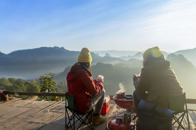 Rear view of people sitting on table against mountains
