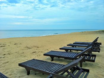 Empty bench on beach against sky