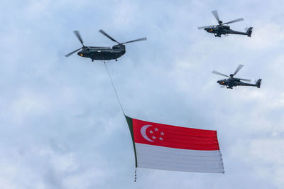 Low angle view of helicopter flying with singaporean flag against sky