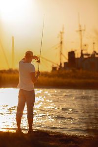 Rear view of man fishing in sea during sunset