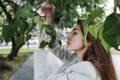 Side view of young woman picking flowers at park