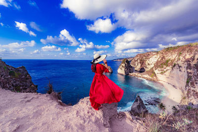 Full length of woman standing on rock by sea against sky