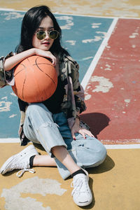 Smiling young woman with basketball sitting on court