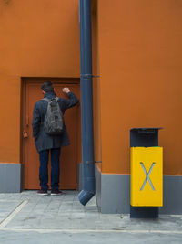 Rear view of man knocking orange door