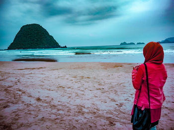 Rear view of woman walking on beach against sky