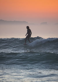 Full length of silhouette man surfing in sea against sky during sunset
