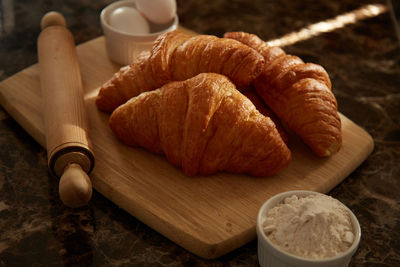 Croissants on a cutting board with a rolling pin and some ingredients close up.