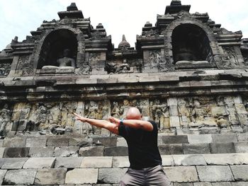 Low angle view of man gesturing against old buddhist temple