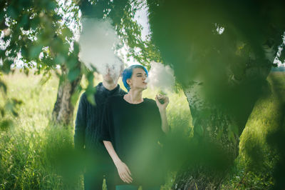 Friends smoking while standing by tree on field