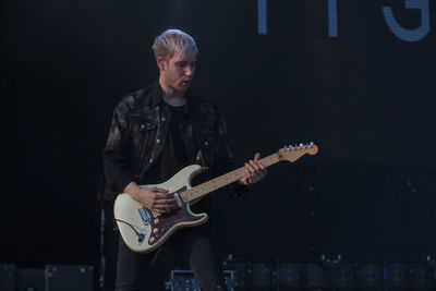 Young man playing guitar against black background